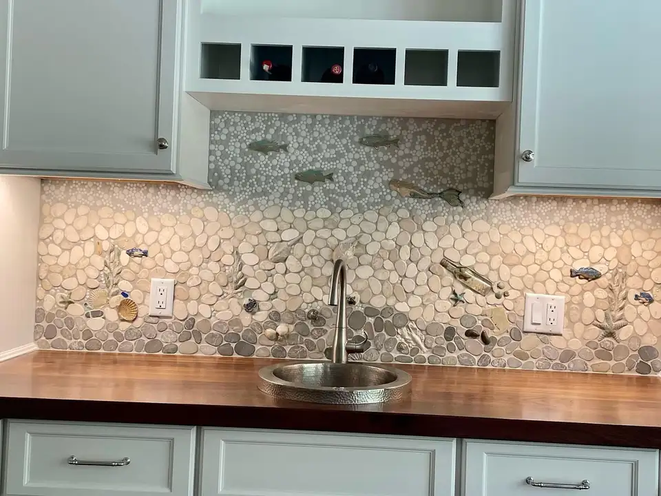 Custom tile in Harwich, MA by Cape Cod Tileworks: pebble mosaic bar backsplash with ceramic fish, a mermaid, shells and starfish above a butcher block counter