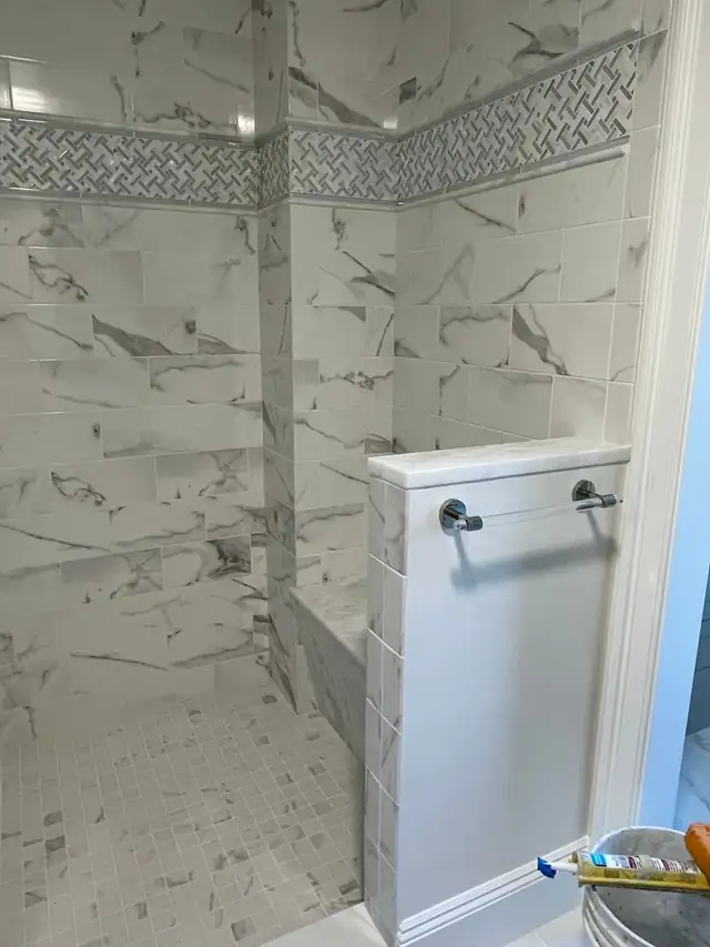 Shower in marble-look porcelain tile with a white half wall and towel bar