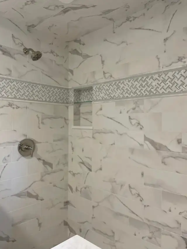 Shower in marble-look porcelain tile with a basketweave mosaic border and recessed niche