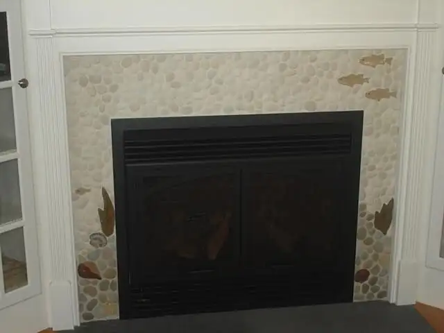 Fireplace surround in cream pebble mosaic with small fish and reed details inside white trim